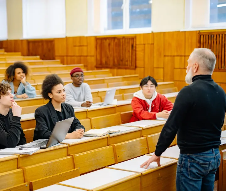 A lecturer talks with a group of students in a wooden lecture hall